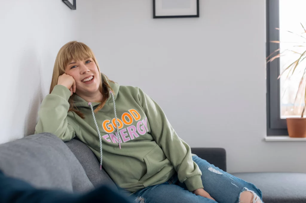 Texterin für Gesunheitscoaches sitzt authentisch und ehrlich auf der Couch und freut sich, deren mehr Zeit und Entlastung zu geben.